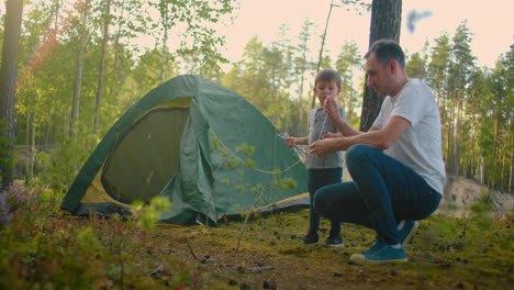 The-boy-helps-his-father-to-set-up-and-assemble-a-tent-in-the-forest.-Teaching-children-and-travelling-together-in-a-tent-camp
